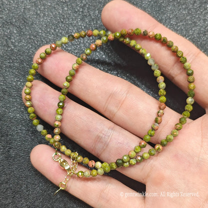 Hand holding 3mm faceted unakite necklace showing green epidote and pink feldspar matrix