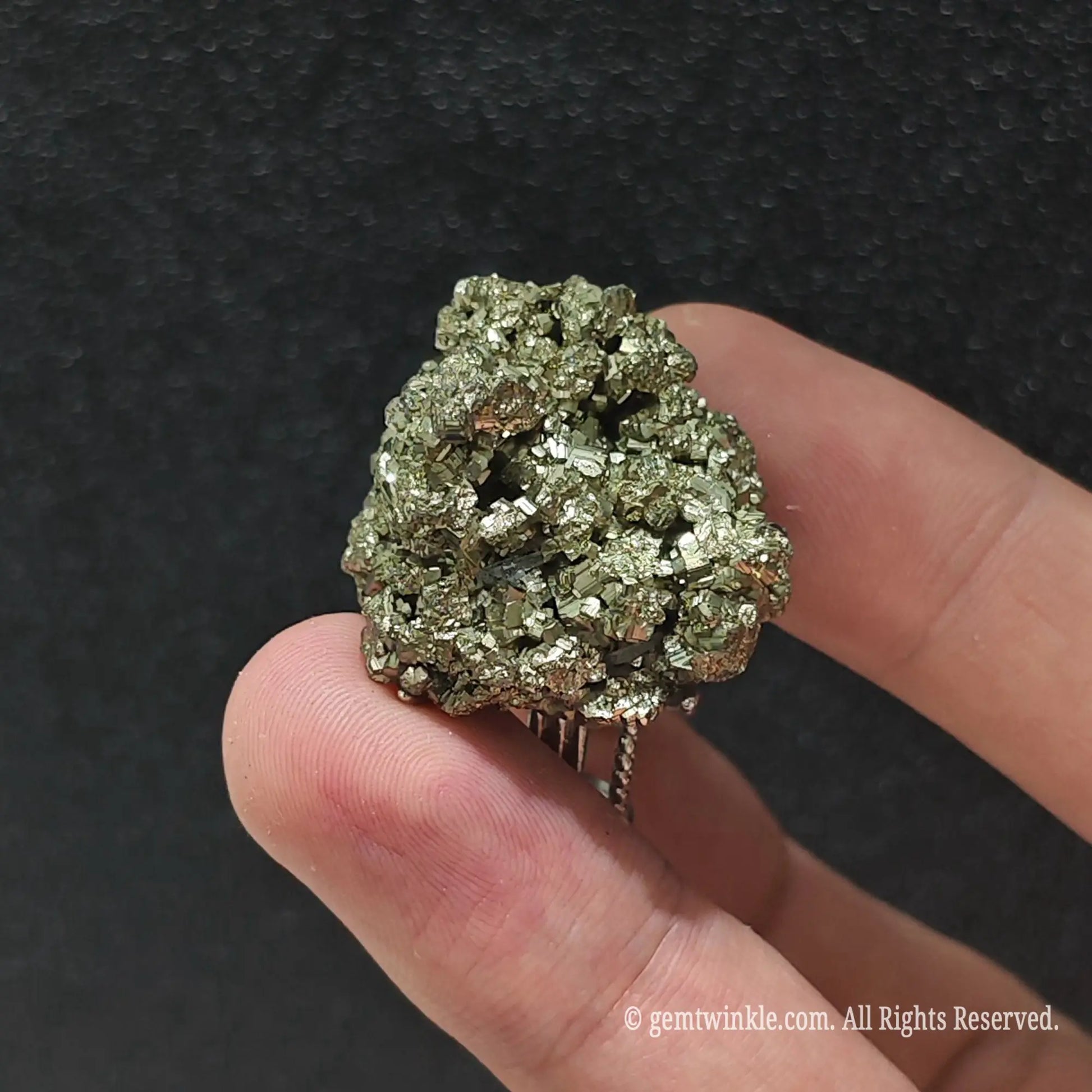 Uncut brass gold pyrite crystal ring held under studio light displaying sparkling metallic luster and raw cluster points