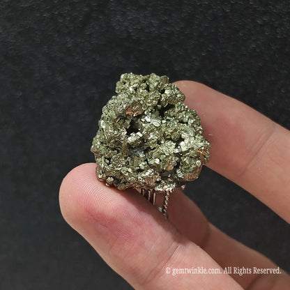 Uncut brass gold pyrite crystal ring held under studio light displaying sparkling metallic luster and raw cluster points