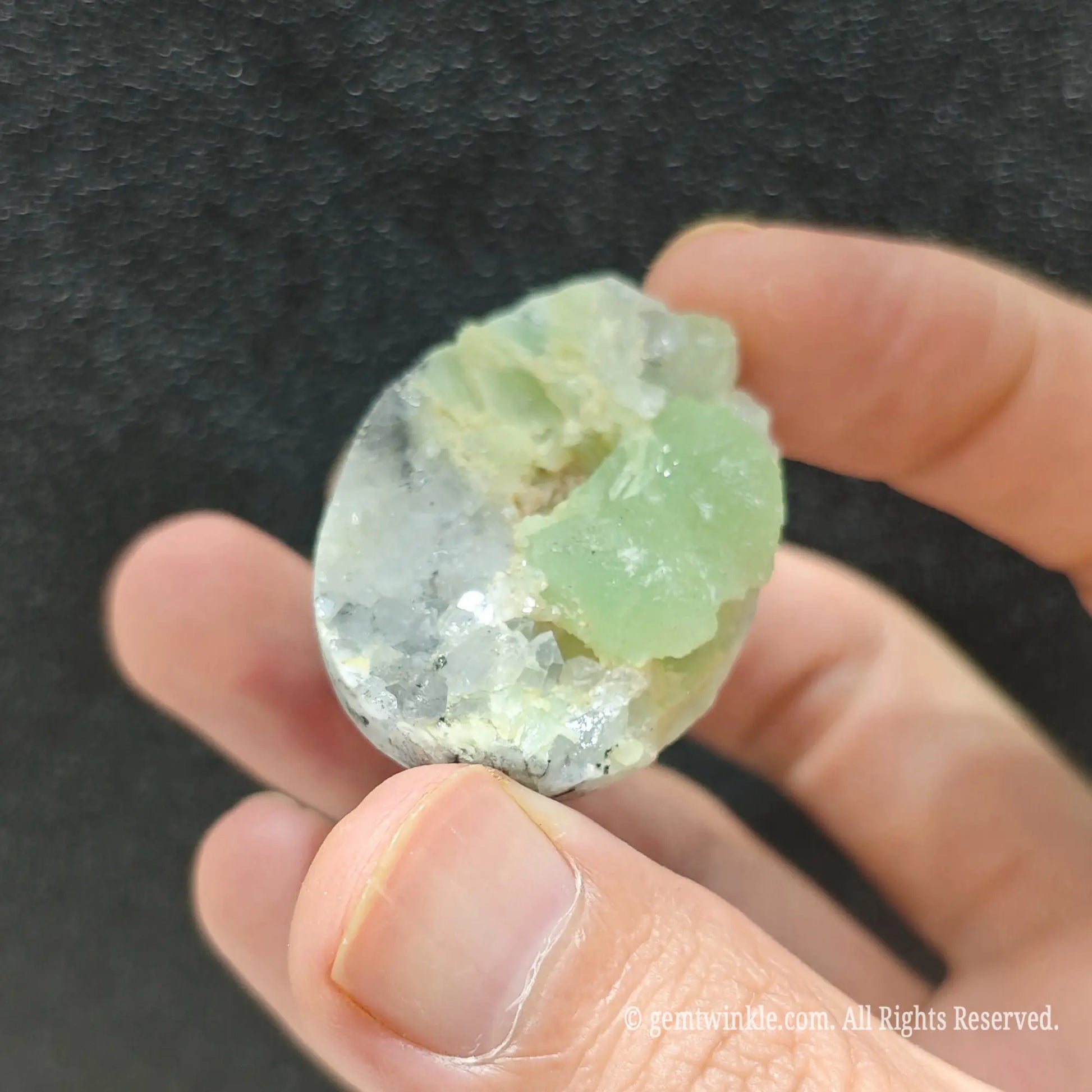 Uncut green fluorite crystal ring held under studio light displaying translucent light green cluster structure