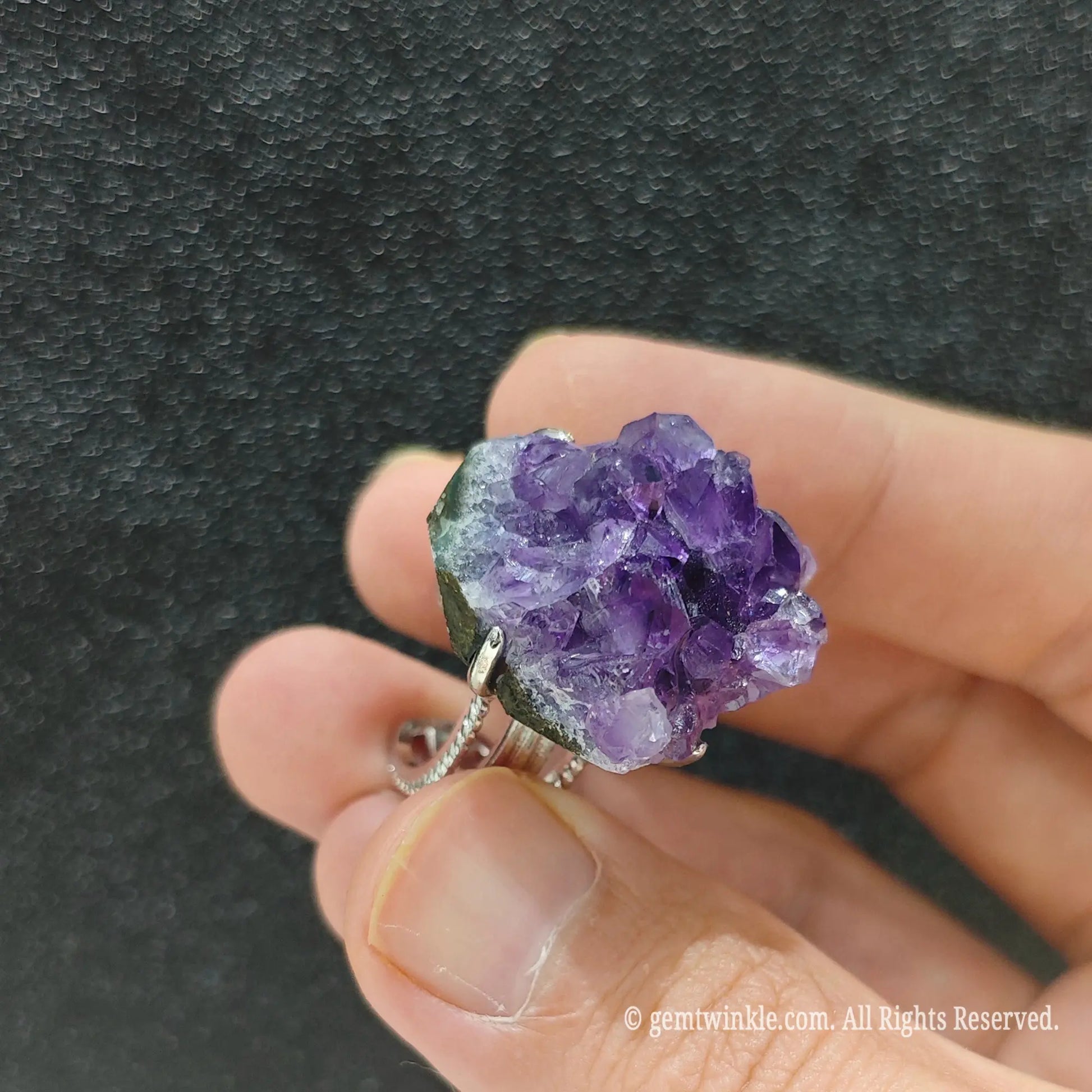Uncut purple amethyst crystal ring held under studio light displaying sparkling royal violet cluster structure