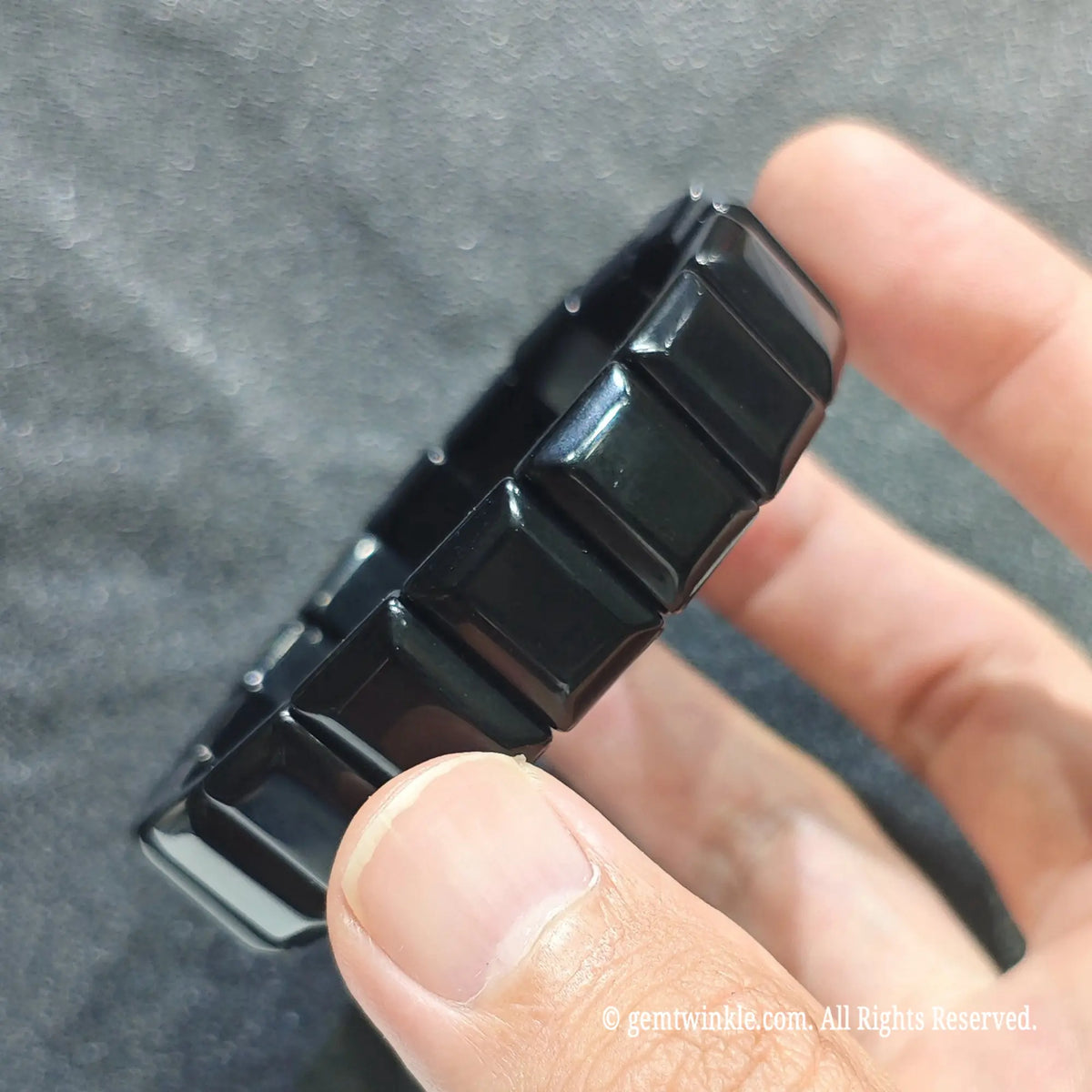Perspective shot of unisex black obsidian plate bracelet resting across fingers under studio lighting