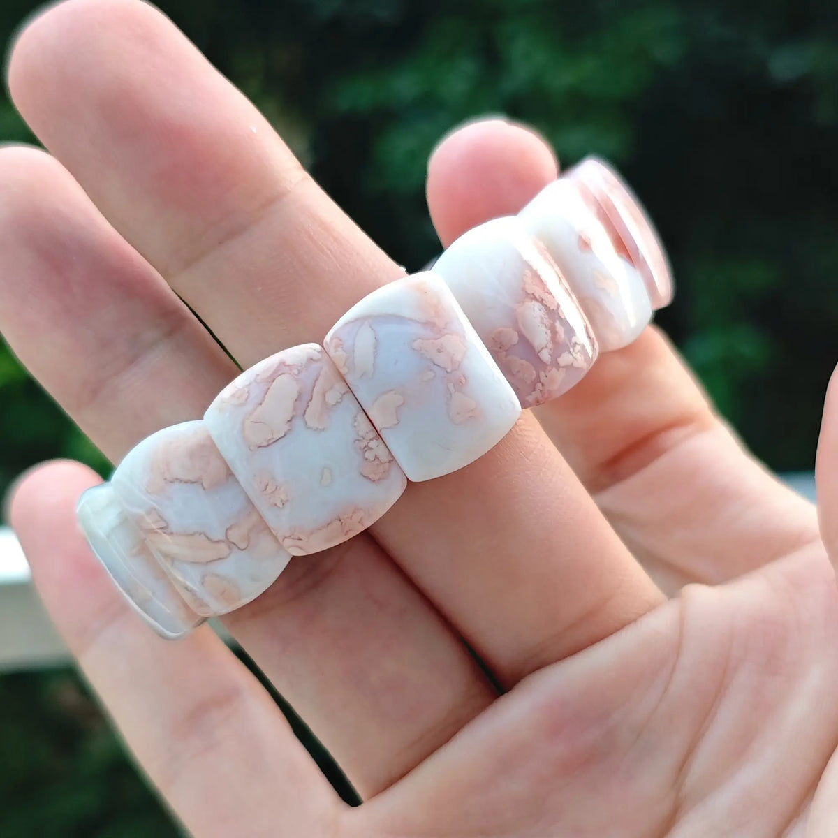 Full view of a unisex natural pink agate gemstone band held in hand displaying smooth vitreous polish