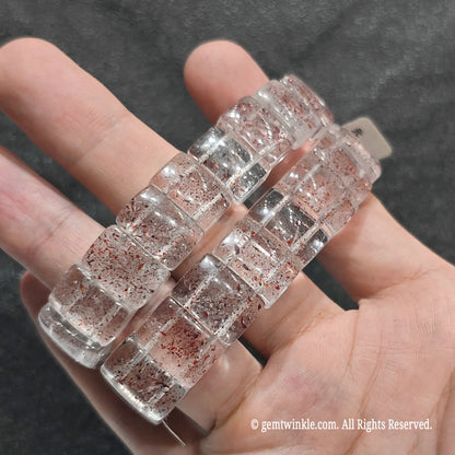 Full view of a unisex natural strawberry quartz gemstone cuff held in hand under bright studio lighting