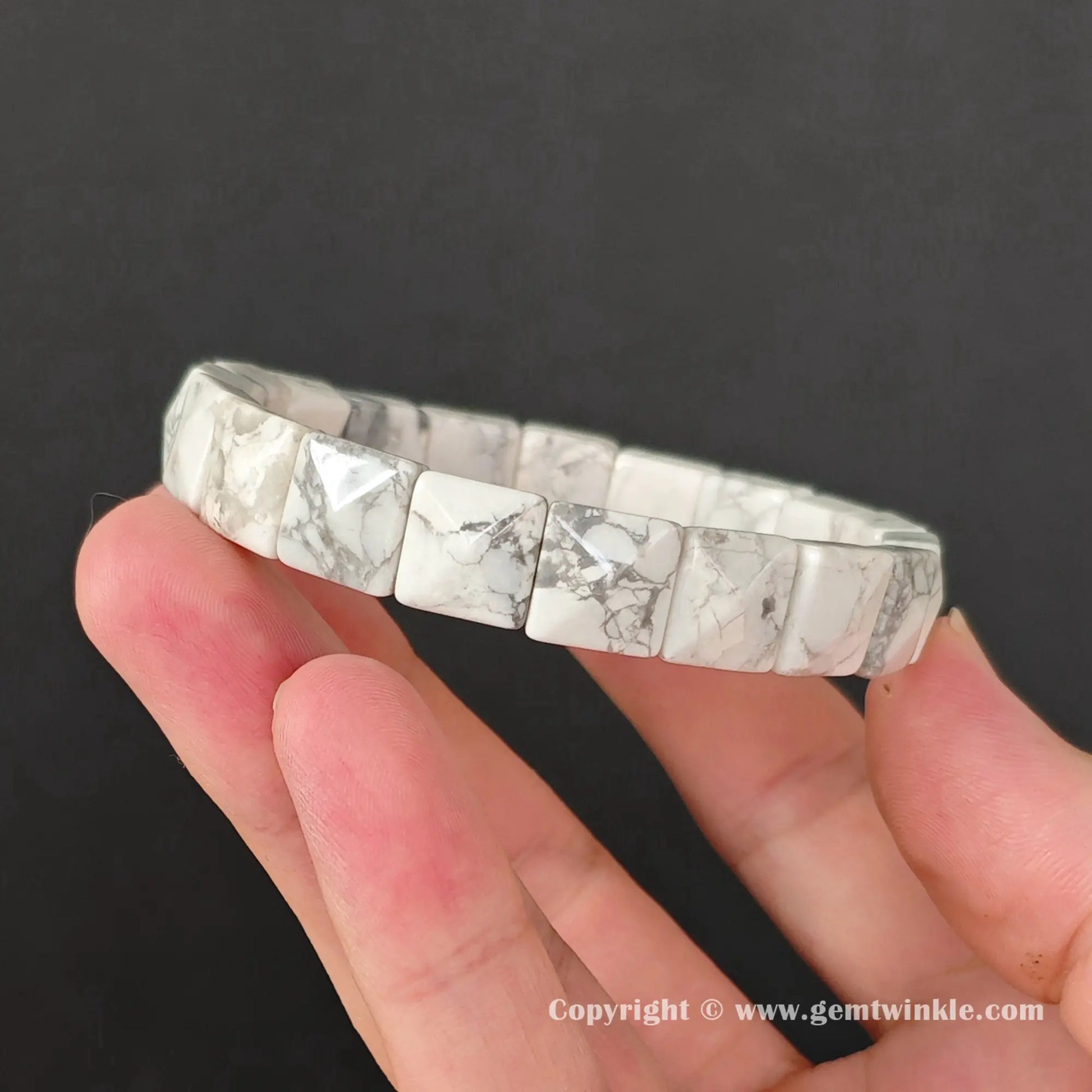 Untreated natural white howlite 10mm slim cuff bracelet held horizontally by fingers