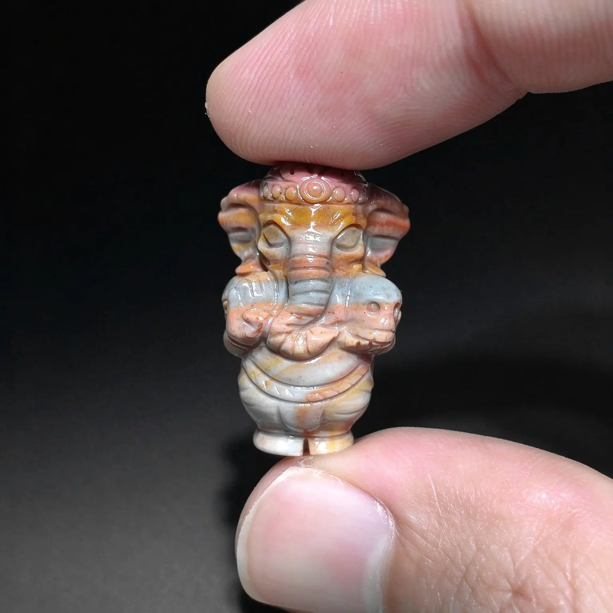 warm red and yellow natural stone ganesha statue mini elephant god figurine held between fingers showing detailed carvings