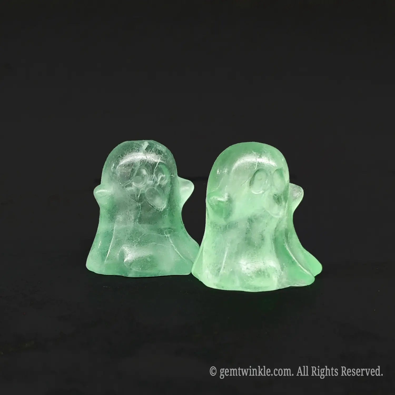 Angled side view of whimsical green fluorite miniature ghost carvings standing on a black background displaying organic internal inclusions