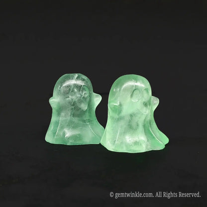 Angled side view of whimsical green fluorite miniature ghost carvings standing on a black background displaying organic internal inclusions