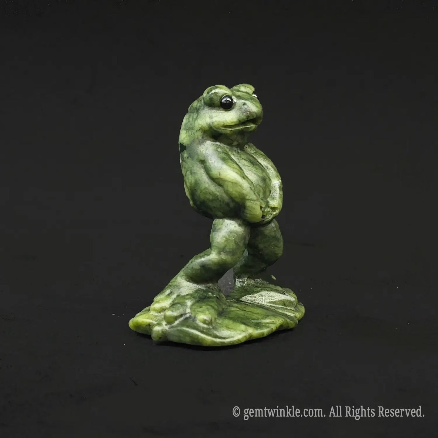 Angled side view of a whimsical serpentine stone manneken pis toad carving showcasing its funny posture on a black background