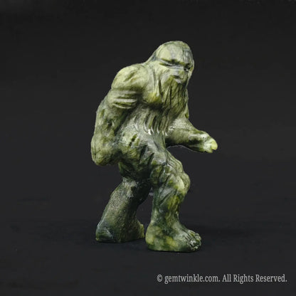 Side angle of a whimsical serpentine stone sasquatch carving displaying mossy olive green yellow fur textures and striding pose