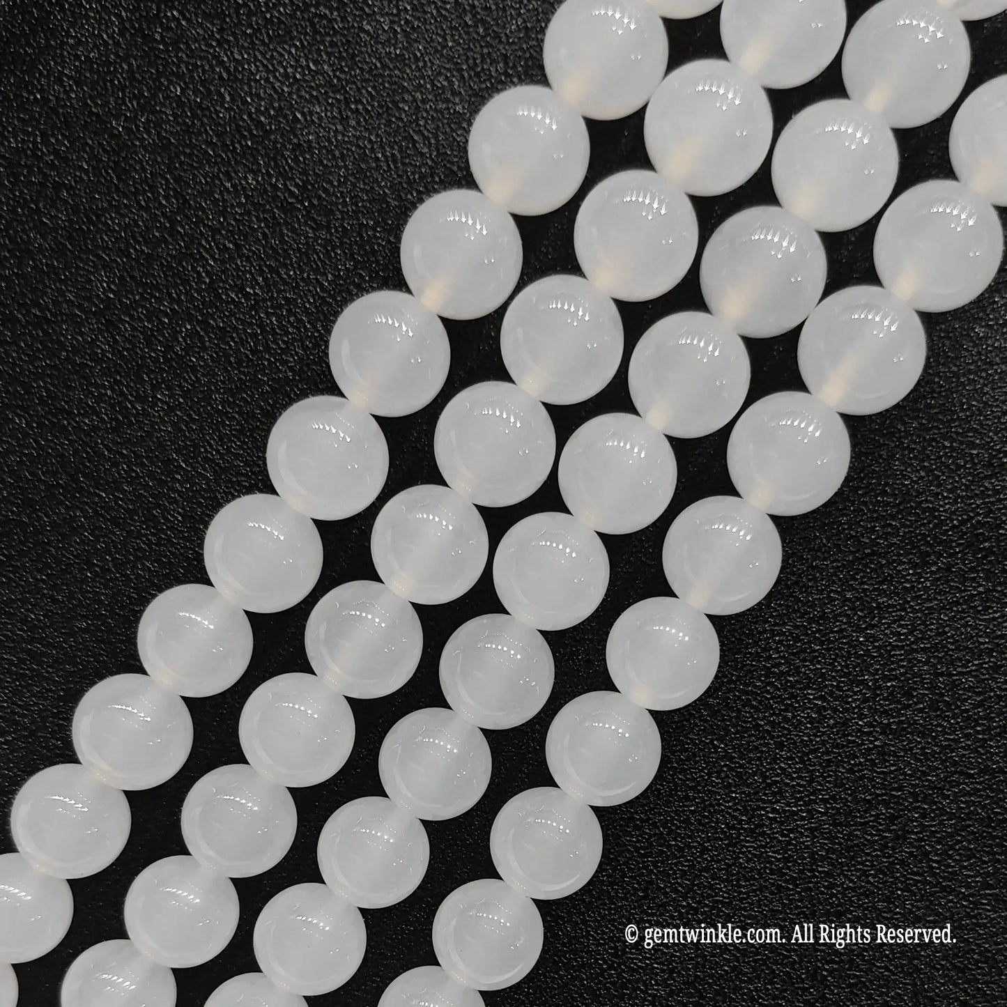 Four strands of natural white chalcedony crystal loose beads aligned on black leather surface