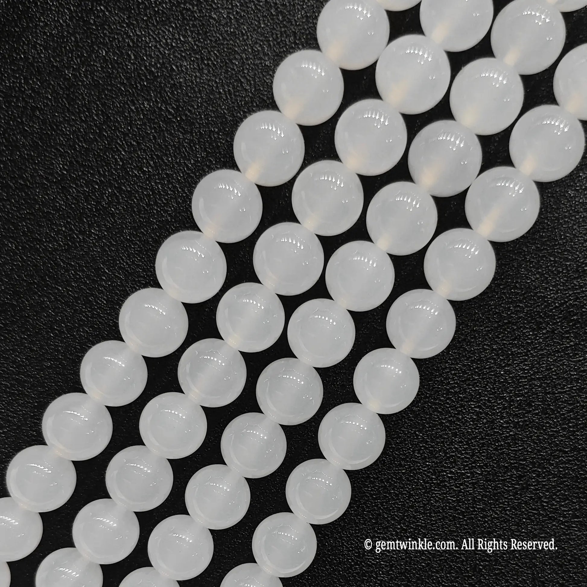 Four strands of natural white chalcedony crystal loose beads aligned on black leather surface