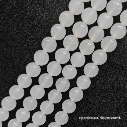 Four strands of natural white chalcedony crystal loose beads aligned on black leather surface