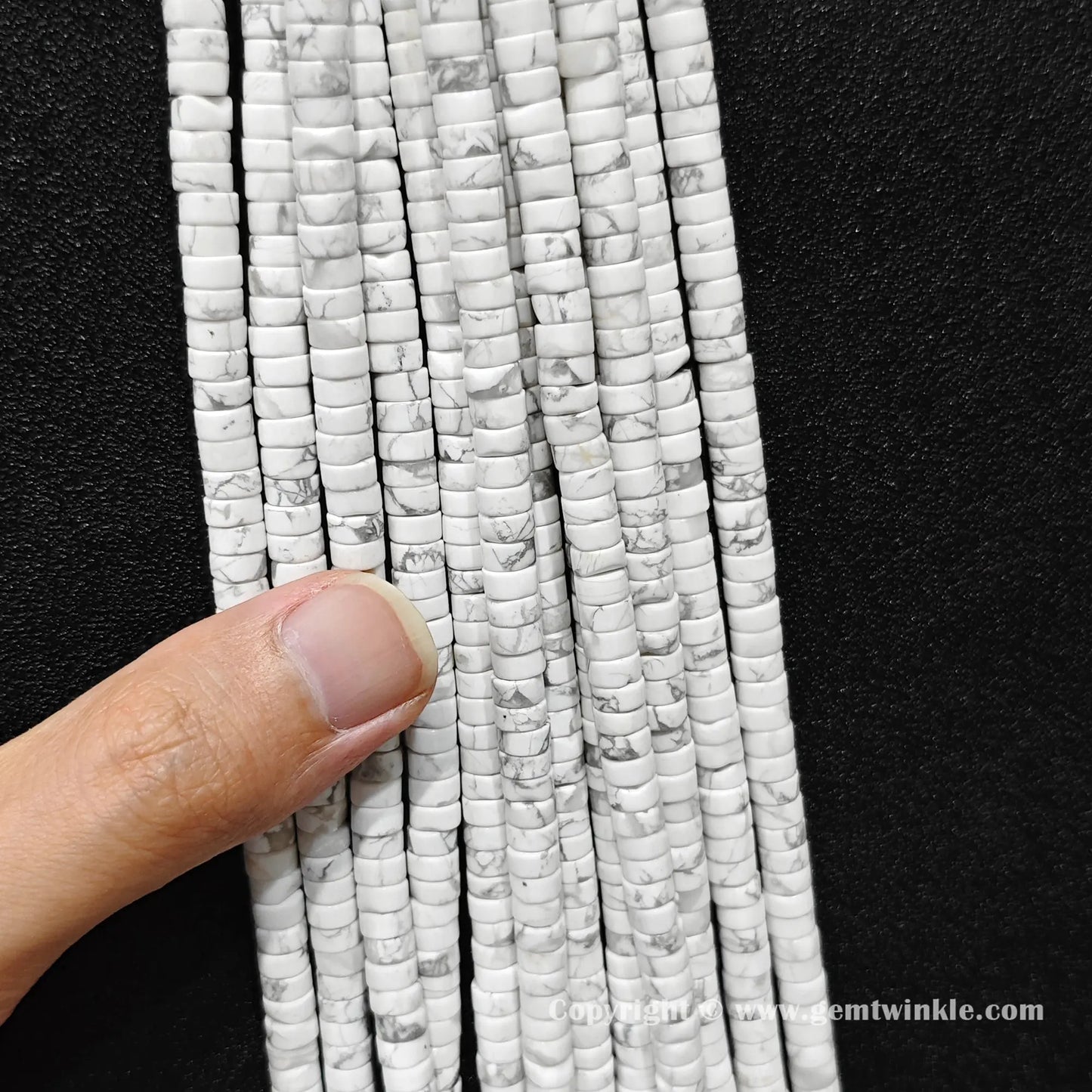 Close up view of 6x3mm white howlite disc rondelle beads held on fingers for quality inspection