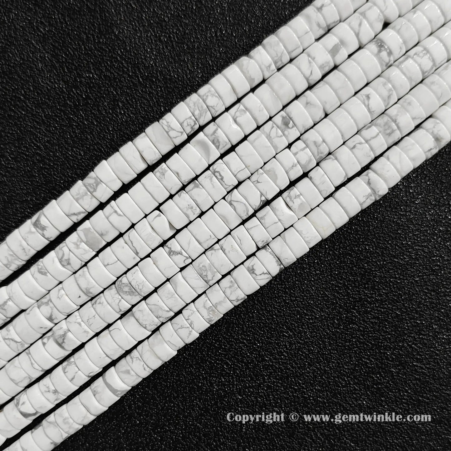 Angled view of white howlite flat disc gemstone strands arranged parallel on dark texture