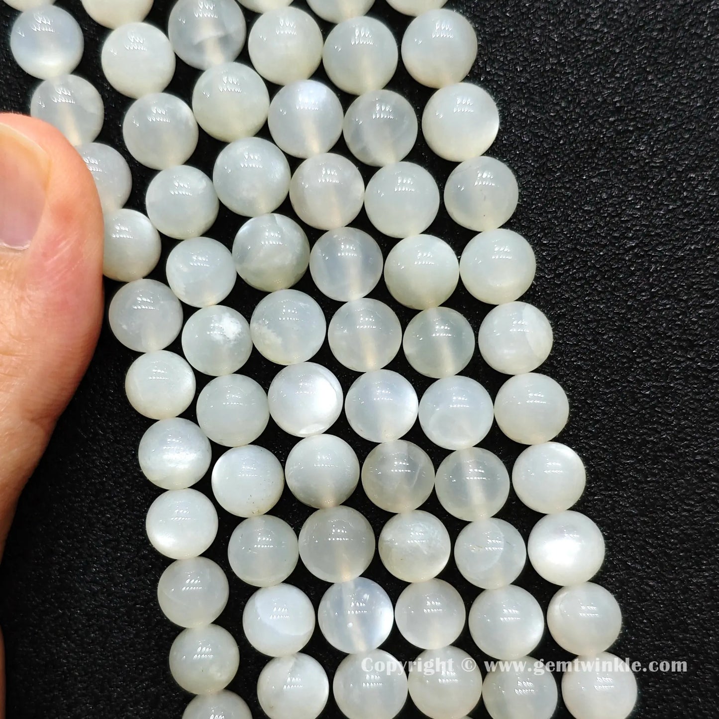 Close up view of white moonstone round beads held on fingers for natural optical sheen preview