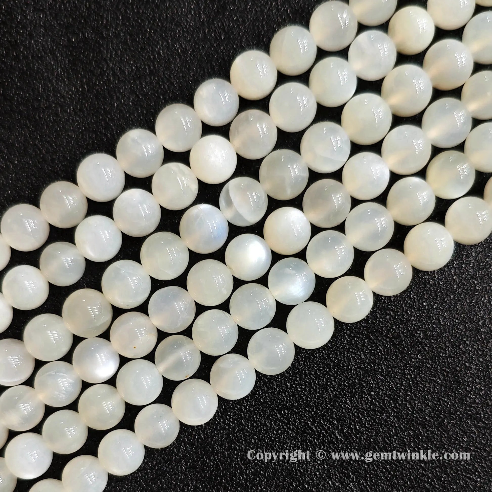 Angled view of white moonstone round bead strands laid parallel on dark textured surface