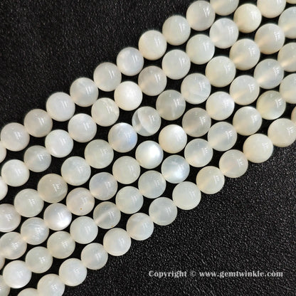 Angled view of white moonstone round bead strands laid parallel on dark textured surface