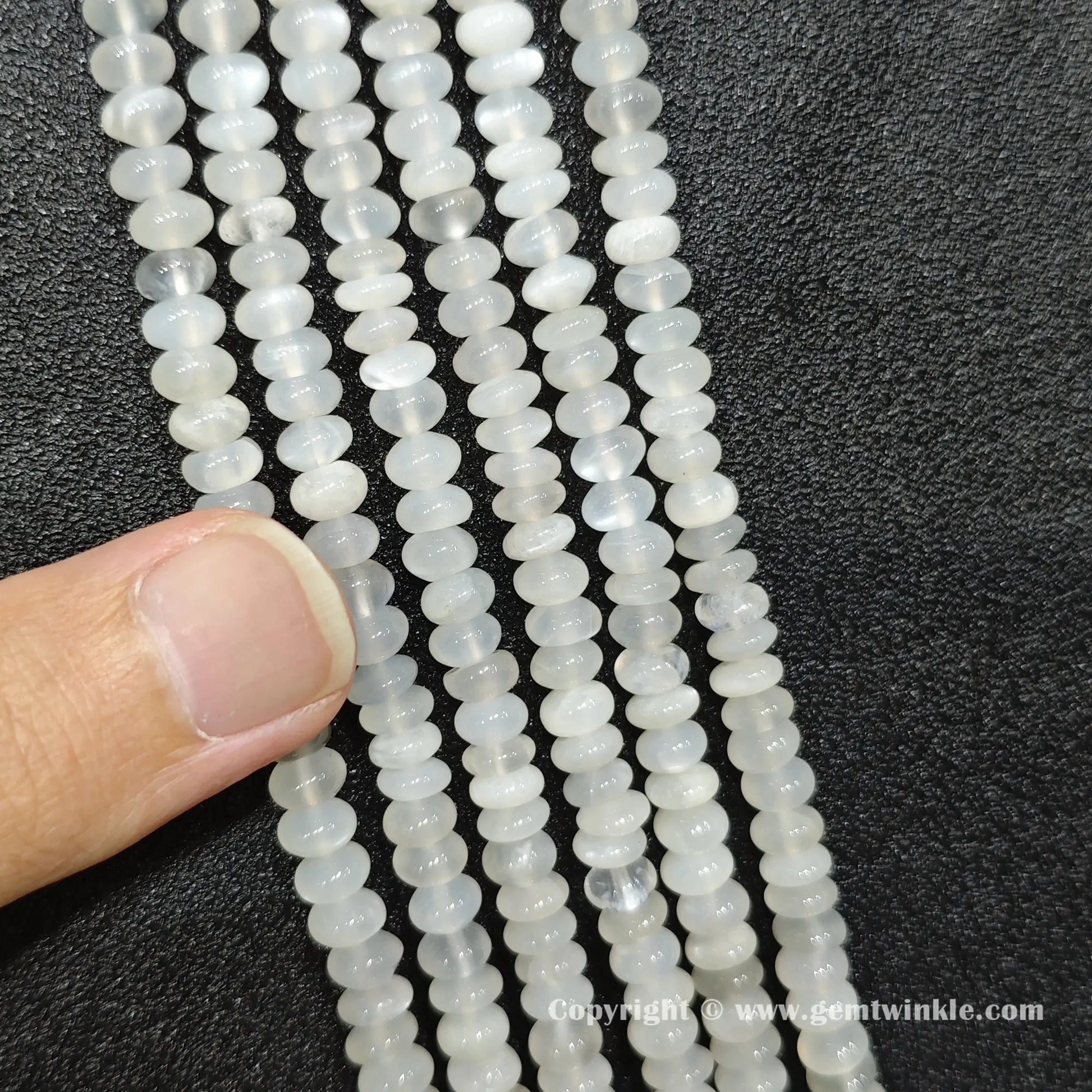 Close up view of 6x4mm white moonstone smooth disc rondelle beads inspected on fingers for quality preview