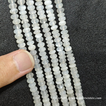 Close up view of 6x4mm white moonstone smooth disc rondelle beads inspected on fingers for quality preview