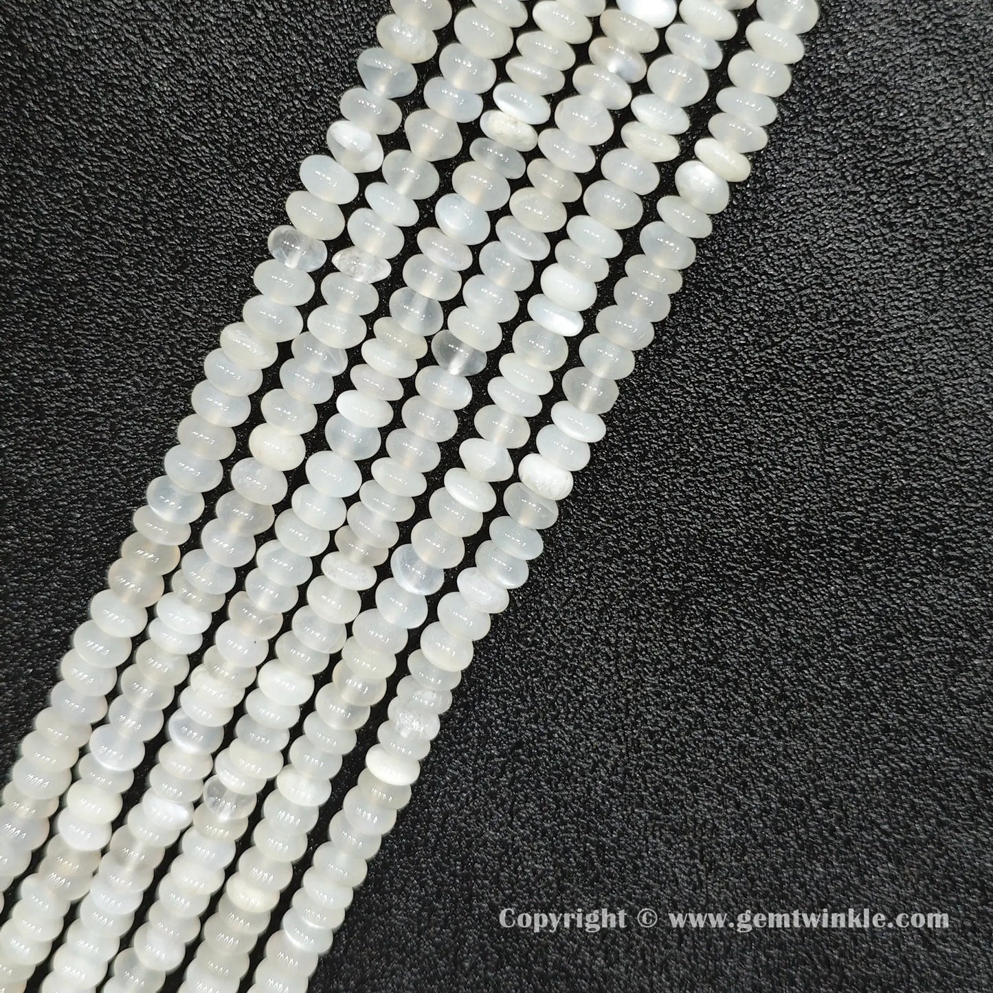 Angled view of natural white moonstone smooth disc gemstone strands arranged parallel on dark background
