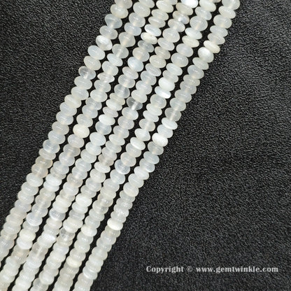 Angled view of natural white moonstone smooth disc gemstone strands arranged parallel on dark background