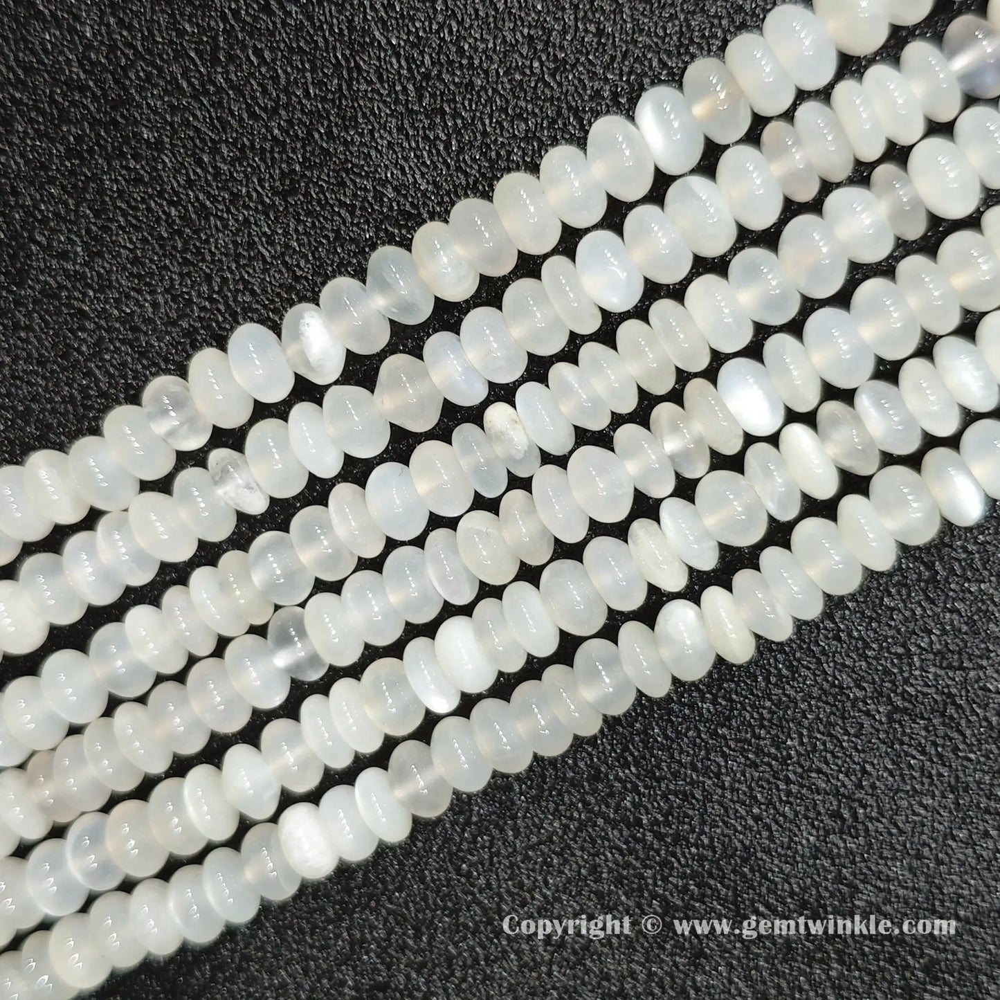 Perspective view of white moonstone smooth heishi spacer beads showing uniform 4mm disc thickness