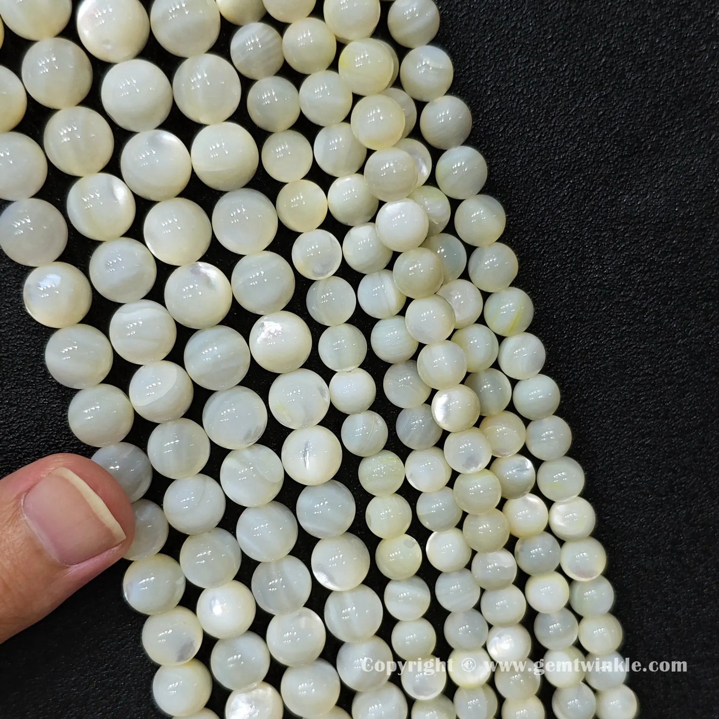 Hand holding white mother of pearl bead strands showing scale and natural organic texture