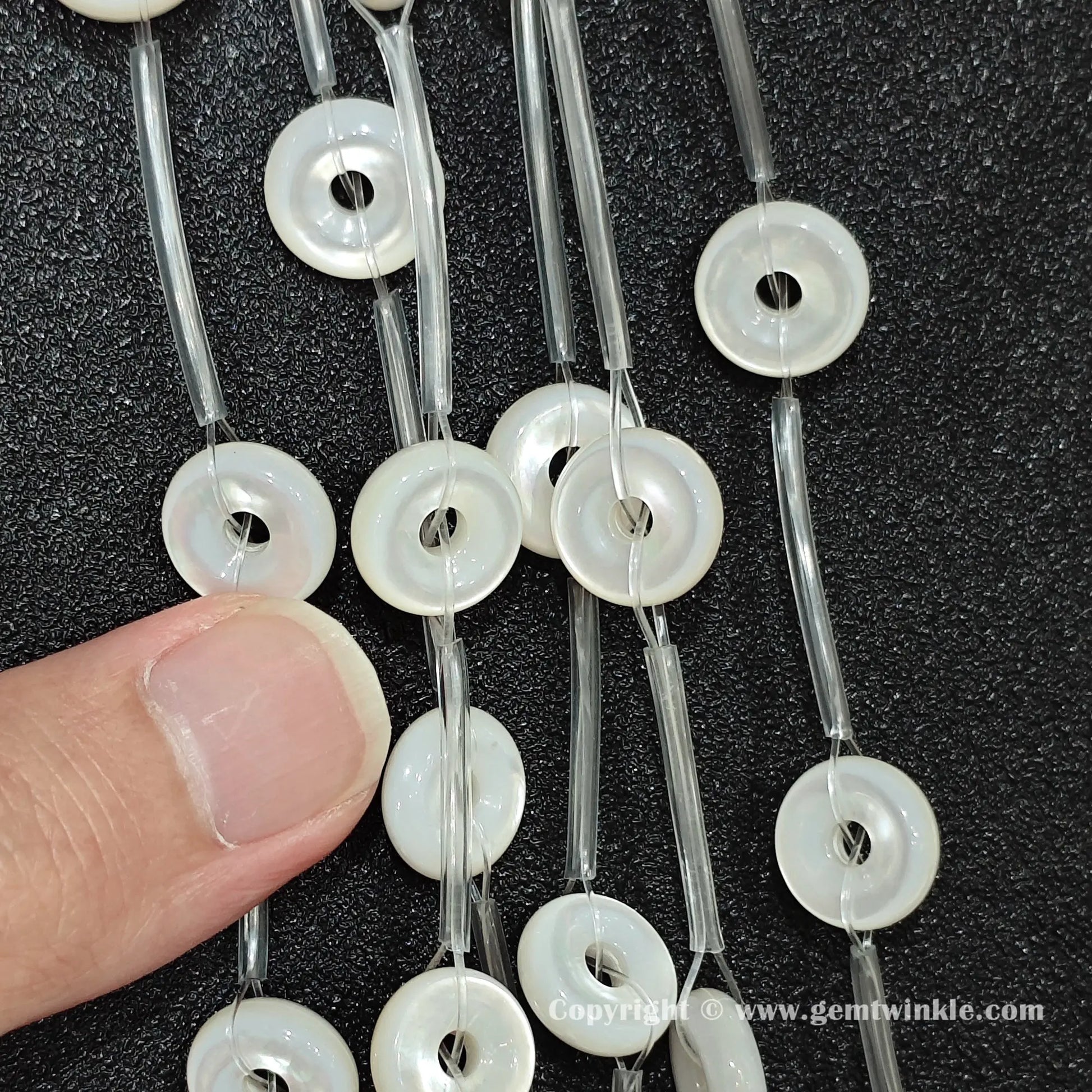 Close up view of white mother of pearl flat ring beads inspected on fingers for quality preview
