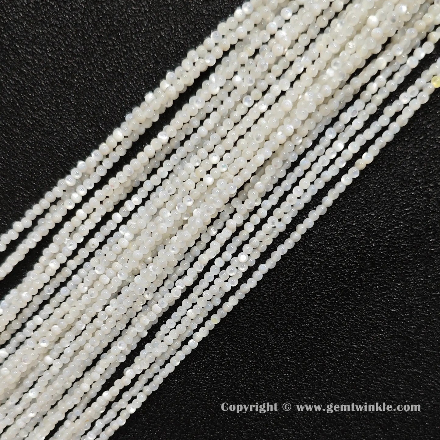 Multiple strands of white mother of pearl small round seed beads lined up on dark background