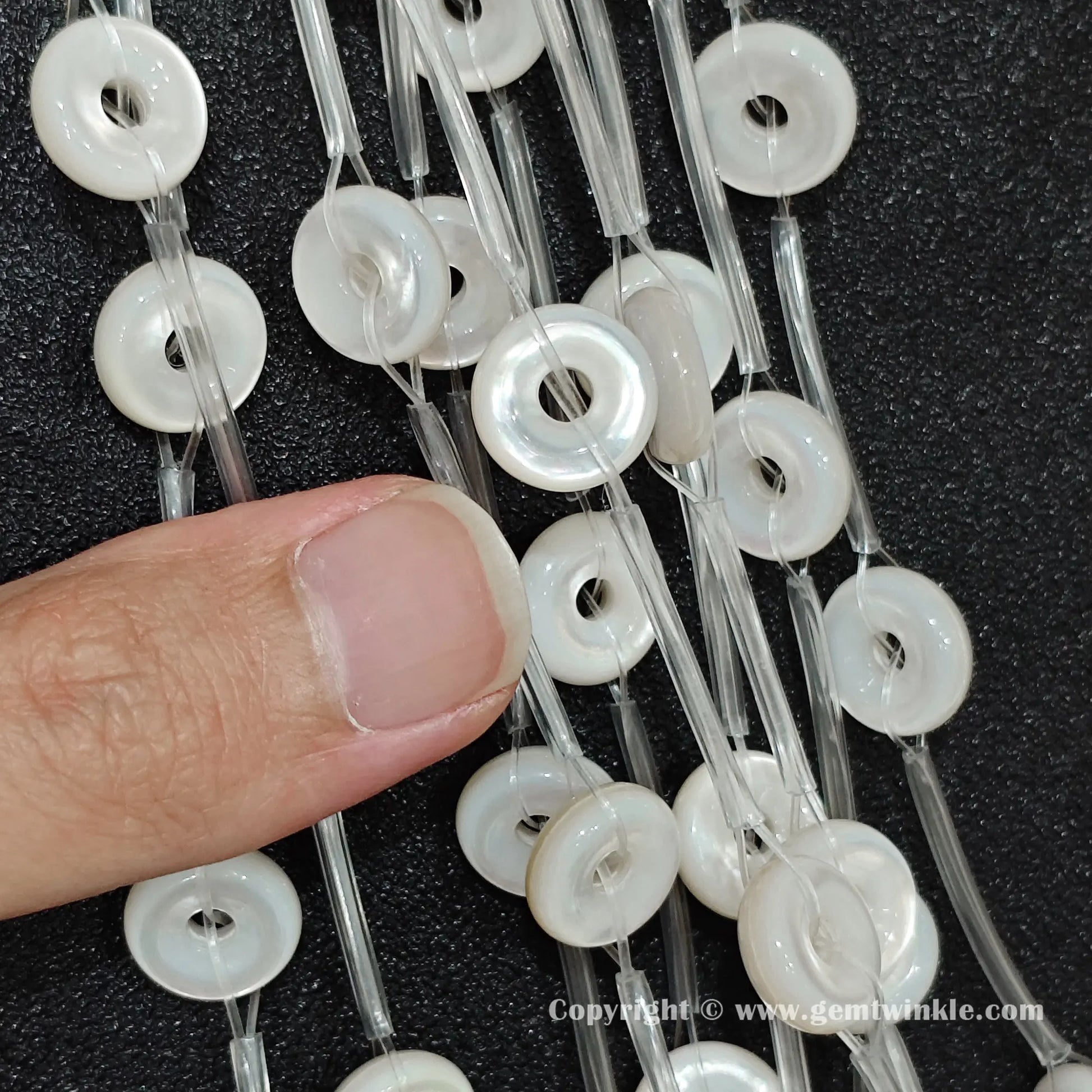 Detailed shot of white shell flat donut washer beads examined against fingertips to display luster