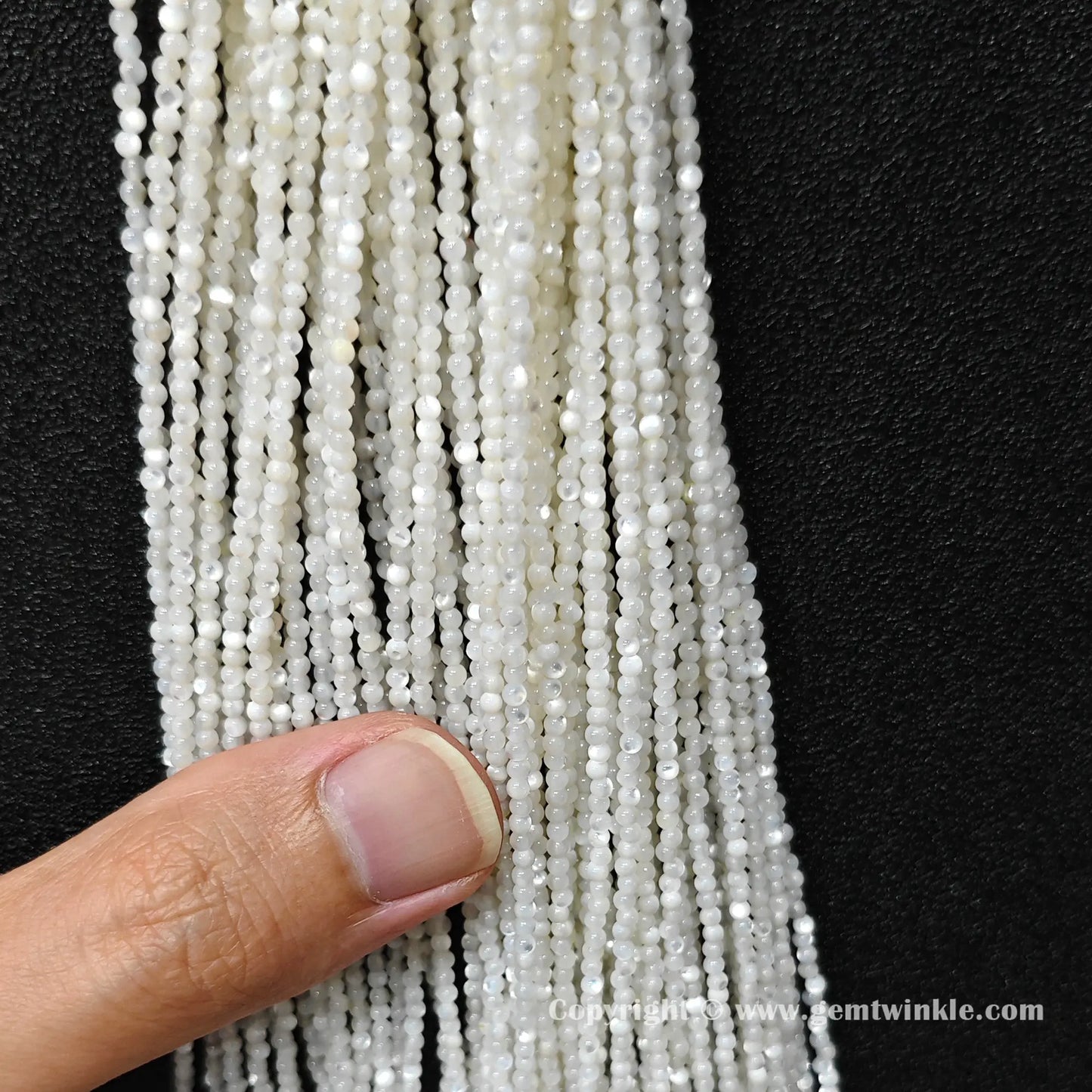 Finger holding white mother of pearl micro seed bead strands demonstrating scale for DIY jewelry