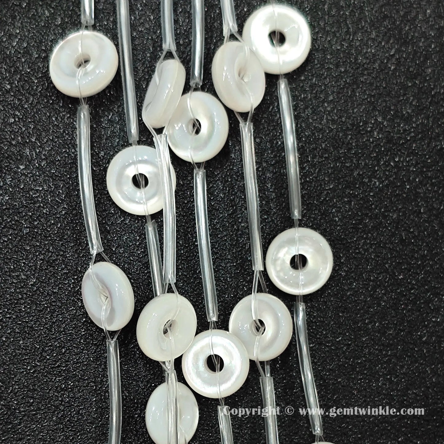 Angled view of natural white shell washer ring beads strung on protective tubes on dark background