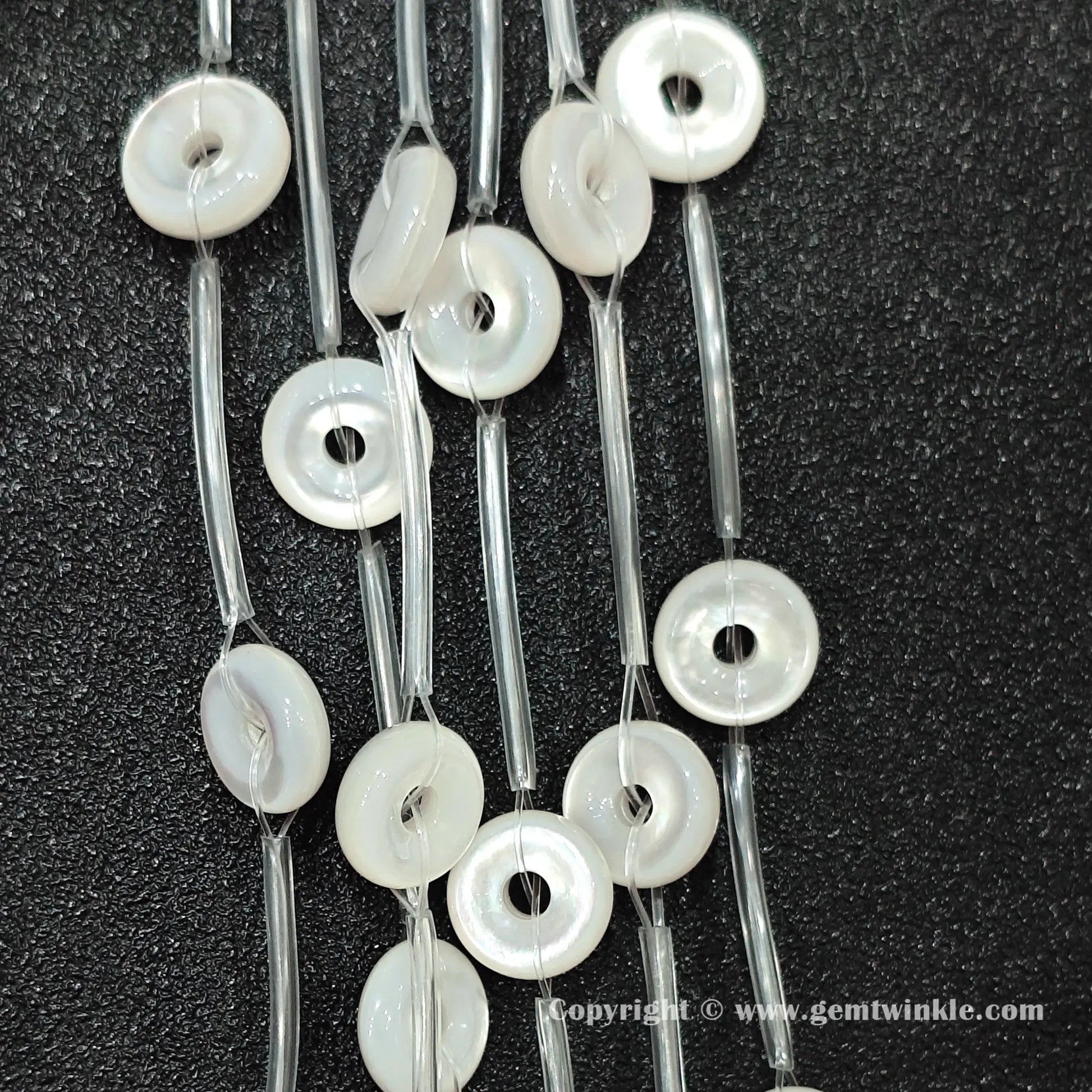 Angled view of natural white shell washer ring beads strung on protective tubes on dark background