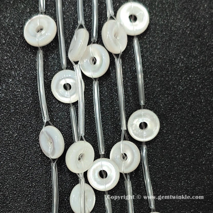 Angled view of natural white shell washer ring beads strung on protective tubes on dark background