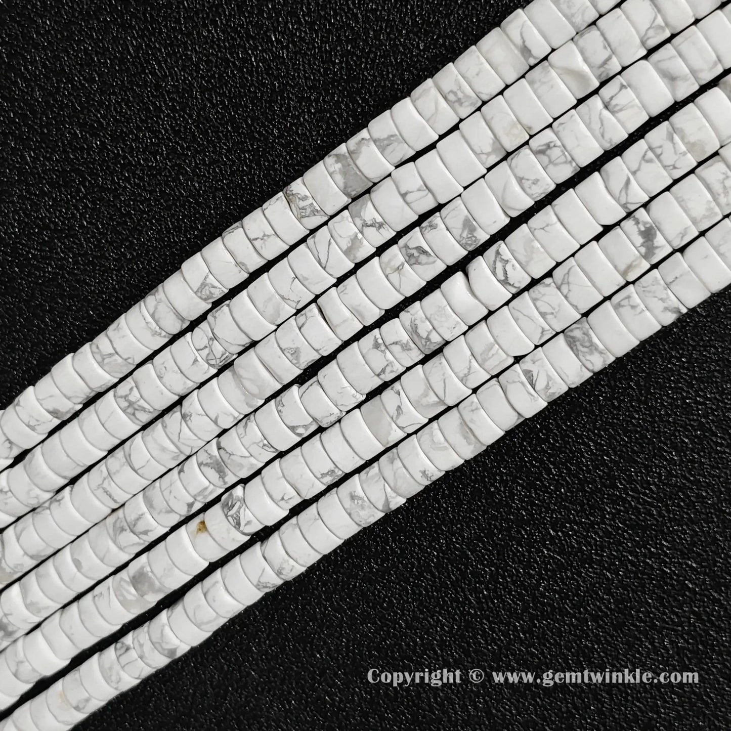 Perspective view of natural white howlite heishi spacer beads showing uniform 3mm thickness