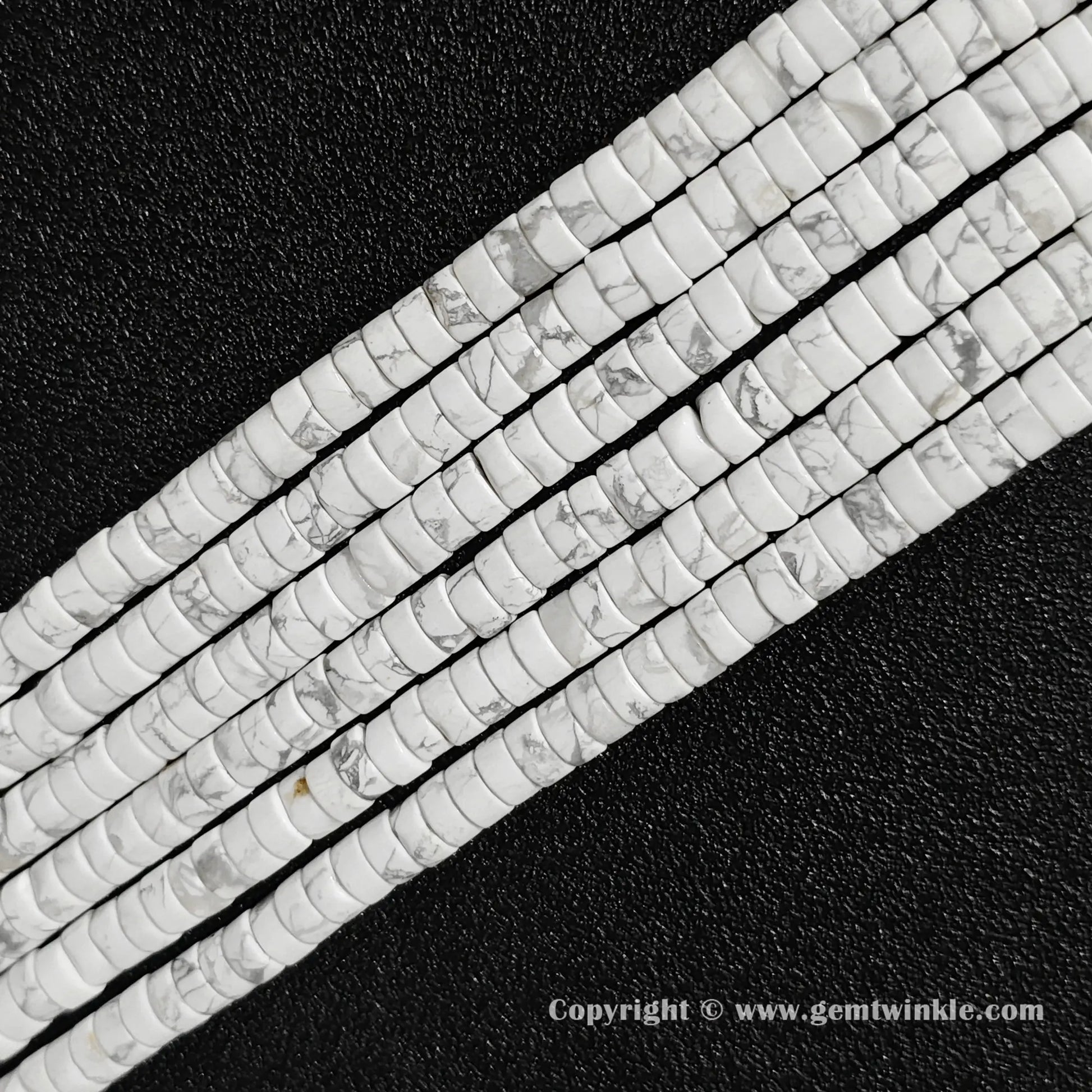 Perspective view of natural white howlite heishi spacer beads showing uniform 3mm thickness