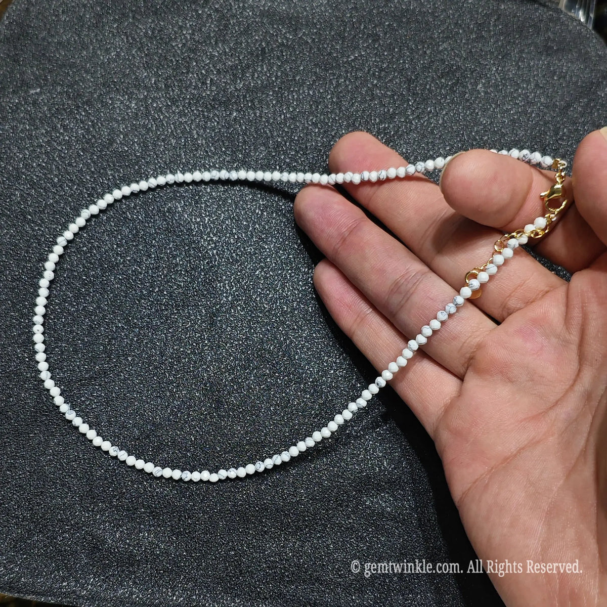 Hand holding 3mm faceted white howlite necklace showing white marble matrix and gold lobster clasp