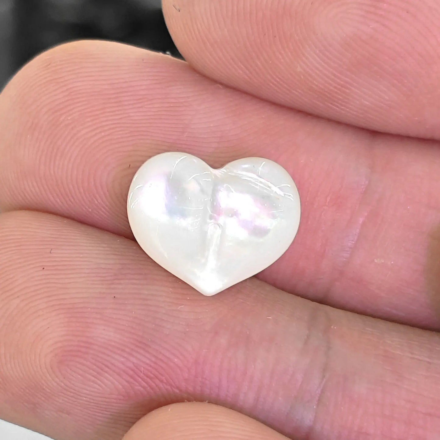 White lip shell 12mm puffy heart bead held in fingers showing natural mother of pearl rainbow sheen