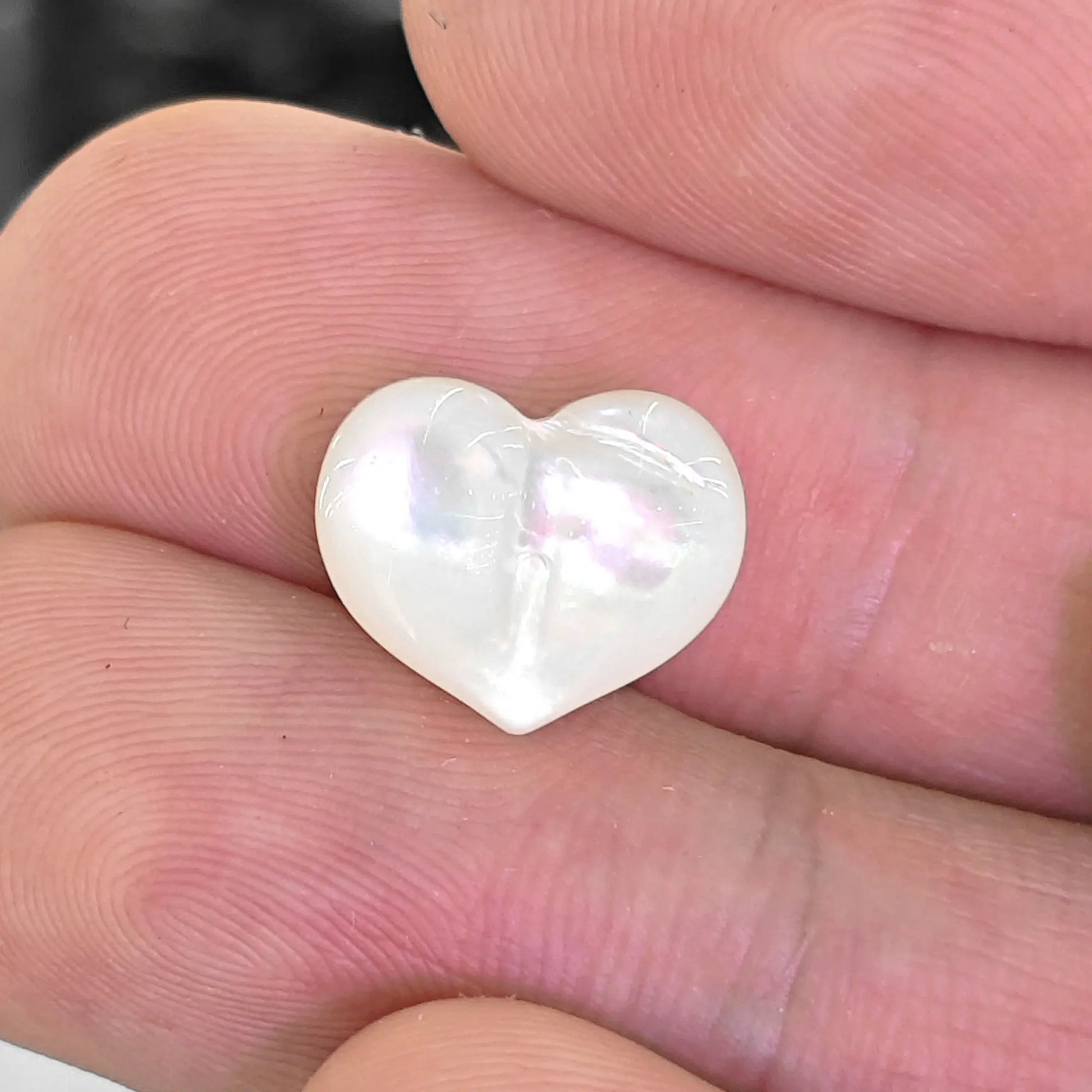White lip shell 12mm puffy heart bead held in fingers showing natural mother of pearl rainbow sheen