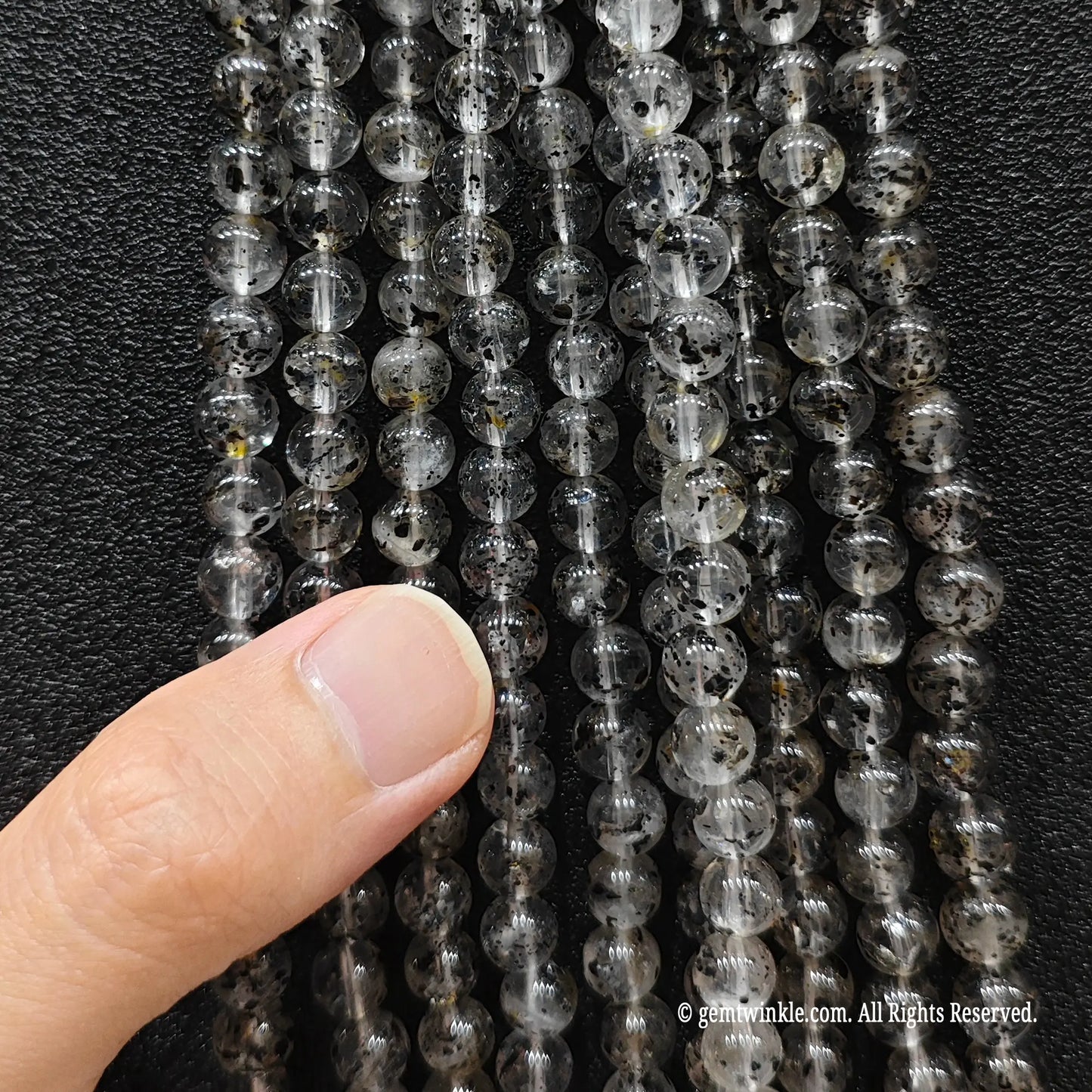 A hand inspecting a collection of black mica biotite quartz strands to check the size choices and polish finish
