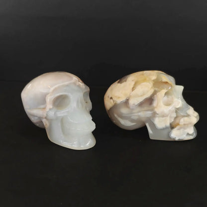 Two natural cherry blossom agate human crystal skull carvings displaying creamy floral chalcedony plumes as shown in image_2928a7.jpg