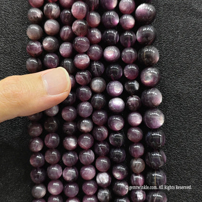 Hand inspecting a collection of purple lepidolite crystal beads strands to show size choices and quality details