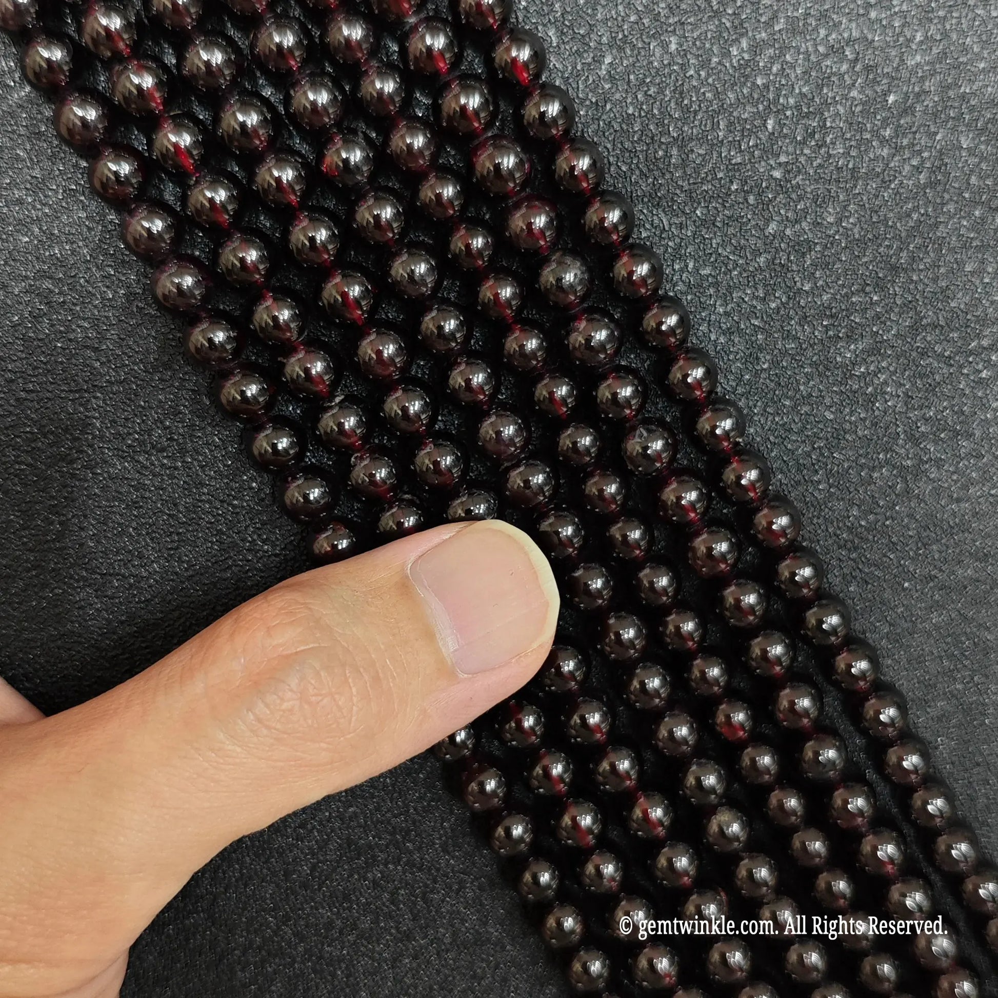 hand checking the polished texture of natural wine red garnet beads