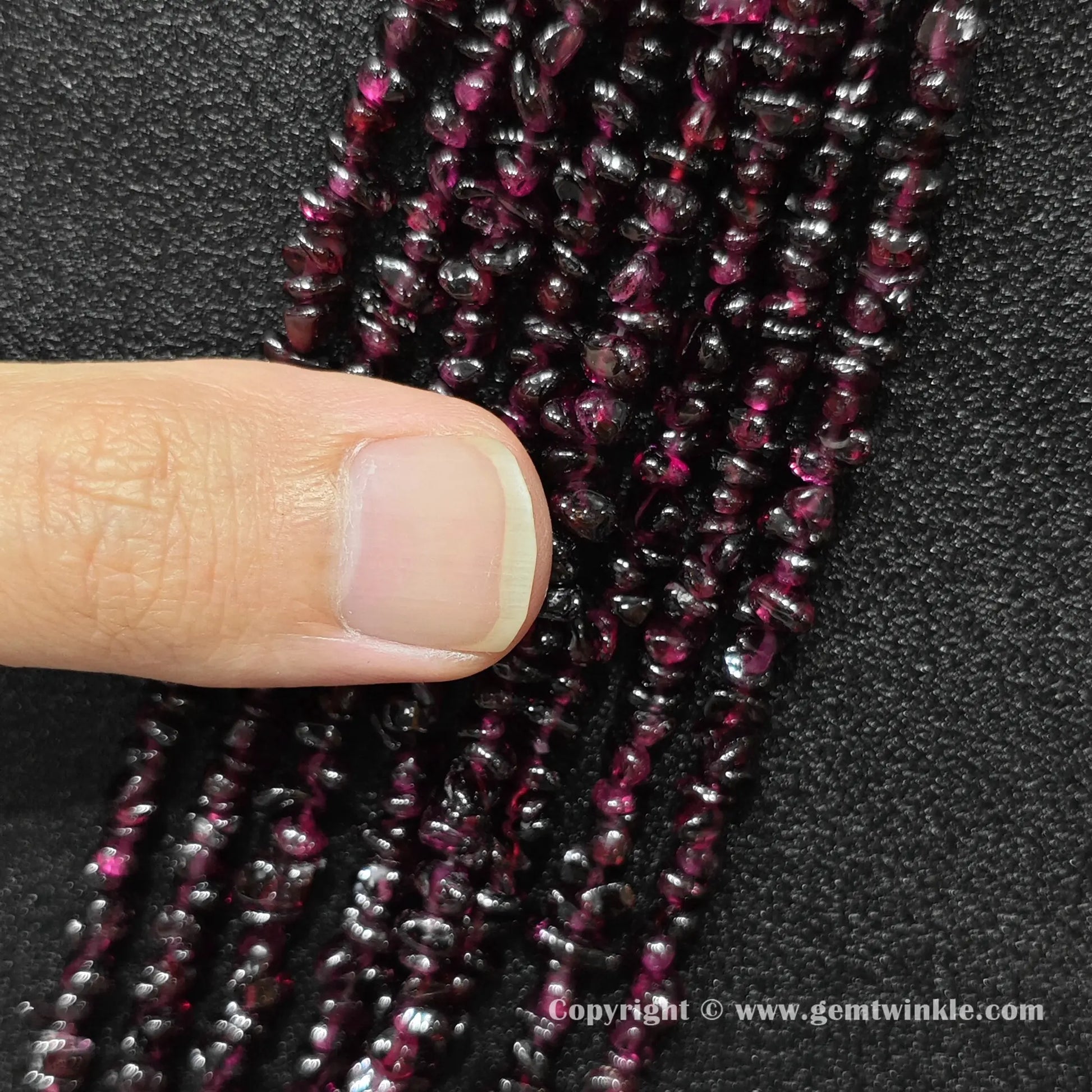 Overview of natural wine red garnet chip bead strands held across fingers