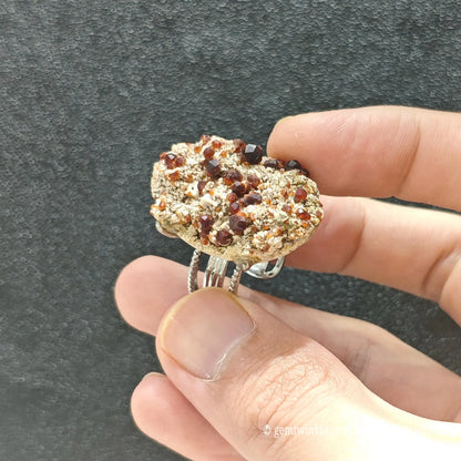 Wine red garnet micro crystal slice ring held under studio light displaying sparkling deep red crystals on natural matrix
