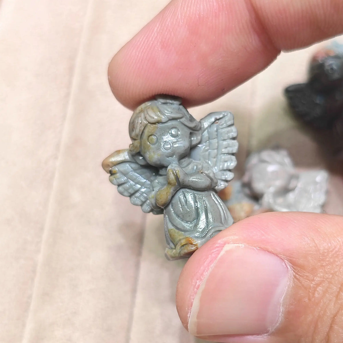 Fingertips holding a small praying cherub statue in muted grey mineral stone showing winged back details