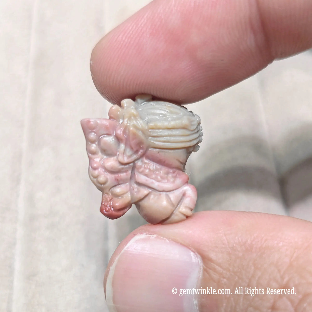Fingertips holding a mini winged fairy statue in warm tan stone showcasing carved wings and held flower