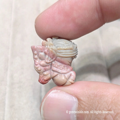Fingertips holding a mini winged fairy statue in warm tan stone showcasing carved wings and held flower
