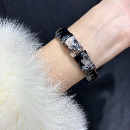 Woman wearing a natural black sakura agate bamboo bracelet on wrist.